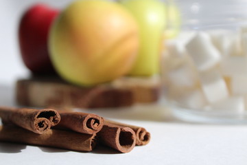cinnamon sticks lie on a white table in the background apples and sugar in a glass jar