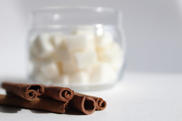 cinnamon sticks close up behind is a jar of sugar on a white background