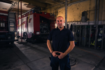 Fototapeta na wymiar Portrait of handsome firefighter standing against trucks at fire station