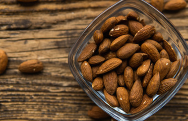 Almonds in a small plate with scattered nuts of almonds around a plate on a vintage wooden table as a background. Almond is a healthy vegetarian protein nutritious food. Natural nuts snacks.