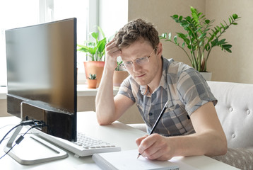 Programmer working from home, remote, home office. A man with glasses looks at the monitor. Remote work concept