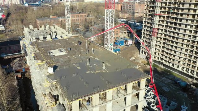 Pouring cement on the floors of residential multi-story building under construction using a concrete pump truck with high boom to supply mixture to upper floors. Aerial high top spone drone view