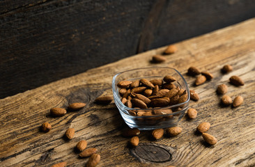 Almonds in a small plate with scattered nuts of almonds around a plate on a vintage wooden table as a background. Almond is a healthy vegetarian protein nutritious food. Natural nuts snacks.