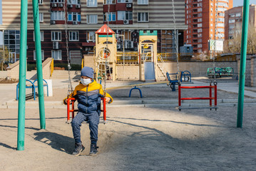 Fototapeta na wymiar A small boy in a mask walks on the Playground during the quarantine. Stay at home