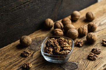 Walnut in a smale plate with scattered shelled nuts and whole nut which standing on a wooden vintage table. Walnuts is a healthy vegetarian protein nutritious food. Walnut on rustic old wood.