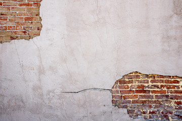 Stucco concrete is broken over an old brick wall with cracks and holes