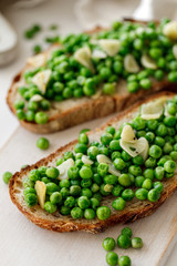 Sourdough bread sandwiches with stewed green peas, olive oil and garlic on a white wooden board close up 