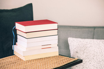 Book stack on the table with cozy sofa, cushions and pillows. Reading books, study at home,...