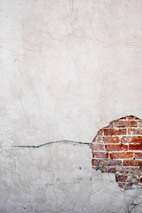 Stucco concrete is broken over an old brick wall with cracks and holes vertical
