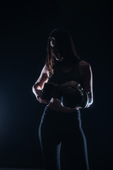 Fototapeta na wymiar Silhouette portrait with dark contrast of a young fitness girl putting on her boxing gloves