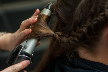 Hairdresser doing a woman's hair in professional hairdressing salon or barbershop , seen from behind the customer, unrecognizable.