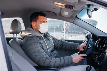 A young man sits behind the wheel wearing a mask for personal safety while driving during a pandemic and coronavirus. Epidemic