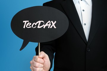 TecDAX. Geschäftsmann im Anzug hält Sprechblase in die Kamera. Der Begriff TecDAX steht im...