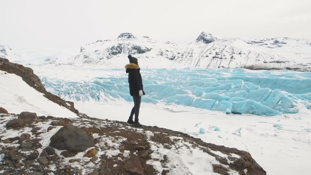 Vatnajokull Icelandic glacier in the mountains. Young woman tourist in a black jacket walks around huge glacier in Iceland.
