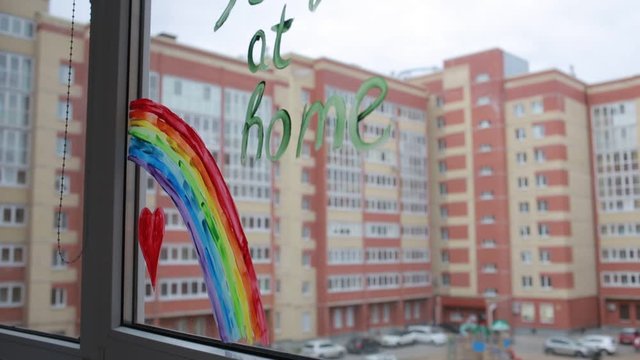 Social media campaign to prevent the covid-19 coronavirus pandemic. Drawing of a rainbow on a window during home quarantine. On the window is written : "stay at home". Outside the window-the city