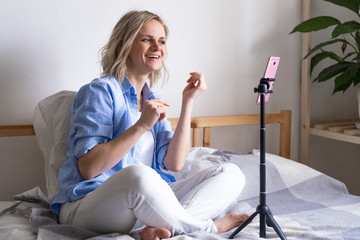 Woman blogger talking with followers, live streaming, looking to smartphone screen sitting on bed....