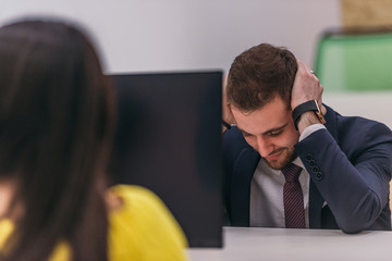 Close-up picture of a male employee being tired of the work and covering his ears with his hands in the office