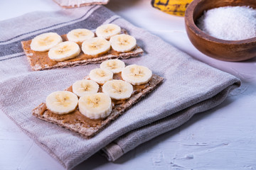 Multi grain crispbread with peanut butter and banana's slices on a cloth. Healthy snack. Swedish bread. Close up view.