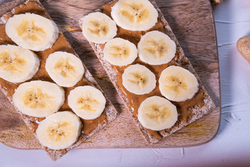 Sesame crispbread with peanut butter and banana's slices on a wooden table. Healthy snack. Sweden product. Top view.