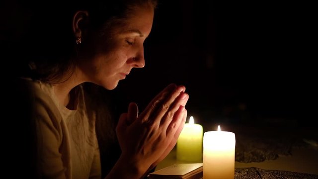 Woman sitting and reading bible verse by candlelight at night, praying close-up