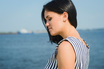 a young brunette girl of European descent in a striped dress walks along the seashore or river