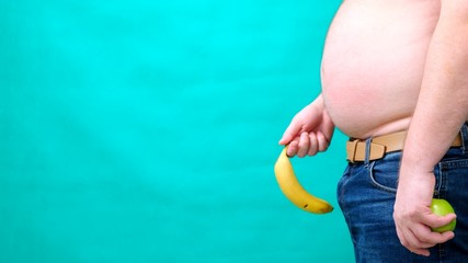 A man with a large belly holds a banana lowered to the bottom of. male sexuality, man sex and...