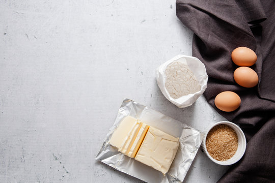 Baking cooking ingredients: a bag of flour, eggs, brown sugar, butter dark linen cloth on light grey concrete background. Top View Copy Space. Cookies Pie Or Cake Recipe Mockup