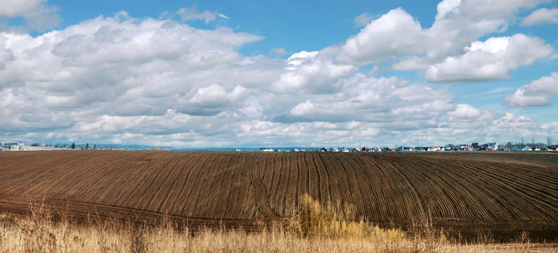 Spring panoramic landscape at border of arable land and farm yardland