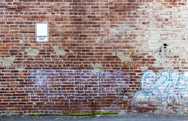 Light white Graffiti on a heavely textured old red brick wall with small white sign over grey asphalt road