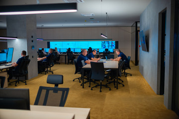 Group of Security data center operators (administrators) working in a group at a CCTV monitoring room while looking at multiple monitors ( computer screens)
