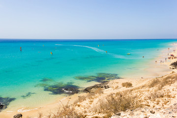 Les gens pratiquent la planche à voile sur une eau turquoise à Fuerteventura, en Espagne. Touristes appréciant les activités de loisirs aux beaux jours près de la plage de Sotavento. Paysage paradisiaque au bord de la mer aux îles Canaries