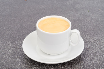 White cup espresso with foam on gray stone background.