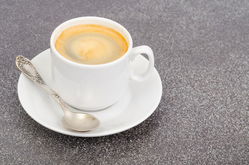 White cup espresso with foam on gray stone background.