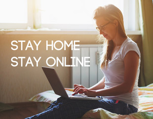 pretty woman with laptop sitting on bed in morning sunlight and typing