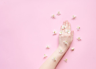 Hands of a woman with white flowers on a pink background. Natural cosmetics product and hand care, moisturizing and wrinkle reduction. Flat Lay and skincare concept.