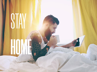 Bearded man lying in bed with morning coffee and digital tablet
