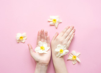 Fototapeta na wymiar Hands and flowers are on a pink background. Natural Cosmetics for hand skin care, a means to reduce wrinkles on hands, moisturizing. Natural cosmetics from flower extract, beauty and fashion