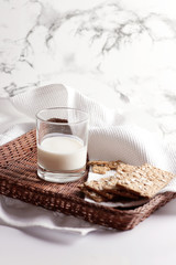 Milk in a transparent glass and healthy cookies with cereals on a cork wood stand. On a marble background.