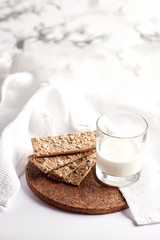 Milk in a transparent glass and healthy cookies with cereals on a cork wood stand. On a marble background.