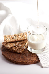 Milk in a transparent glass and healthy cookies with cereals on a cork wood stand. On a marble background.