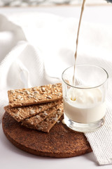 Milk in a transparent glass and healthy cookies with cereals on a cork wood stand. On a marble background.