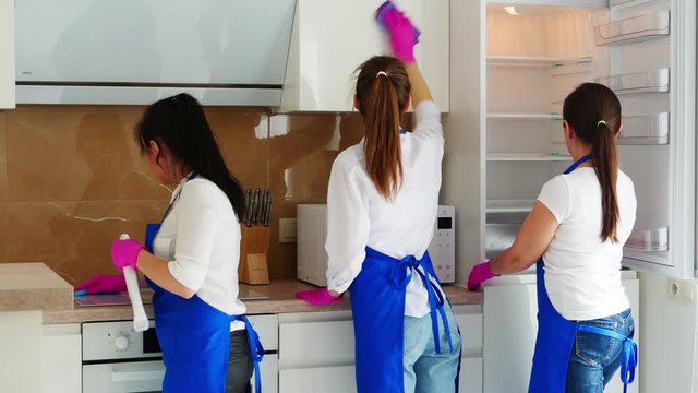 Three beautiful young girls stand with their backs and do the cleaning of the kitchen. Sink chill, oven and cupboards. Professional cleaning.