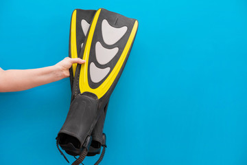 Swimming flippers in a hand on a blue uniform background. Immersion in water. Preparation for holidays and sales in shops, travel companies for tourists and travelers © Amarievikka