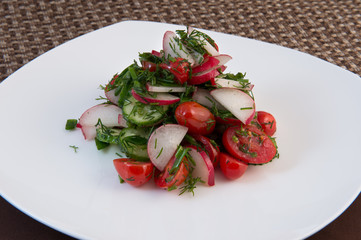 Traditional salad of tomato, cucumber, radish, dill with vegetable oil on a white plate on a brown background