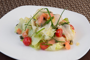 Fresh young cabbage salad with slices of salmon, tomato and onion feathers on a large white plate