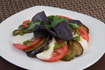 Fried eggplant and zucchini sliced with plastics along with tomatoes, cheese, sprinkled with sauce and decorated with basil parsley