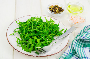 Vegetarian food. Fresh green arugula on plate, white wooden background.
