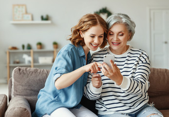 Cheerful mother and daughter using smartphone on sofa.