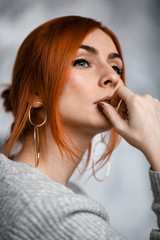 close-up close-up redheaded young woman in a grey sweatshirt with an open shoulder poses and looks thoughtfully away