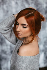 close-up a redheaded young woman in a grey sweatshirt with her shoulder open poses with her eyes closed